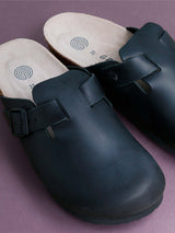 Zueco Genuins Riva de piel engrasada color negro con planta anatómica de caucho corcho y hebilla ajustable metálica para hombre bodegoón